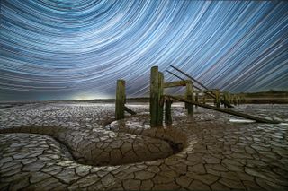 This image was taken at Snettisham Beach, famous for its vast tidal mudflats that attract migrating birds in staggering numbers. The foreground subject is a dilapidated jetty, which was built in the Second World War to allow gravel extracted from the nearby pits to be moved by boat. The curved channel in the mudflat mirrors the trailing stars