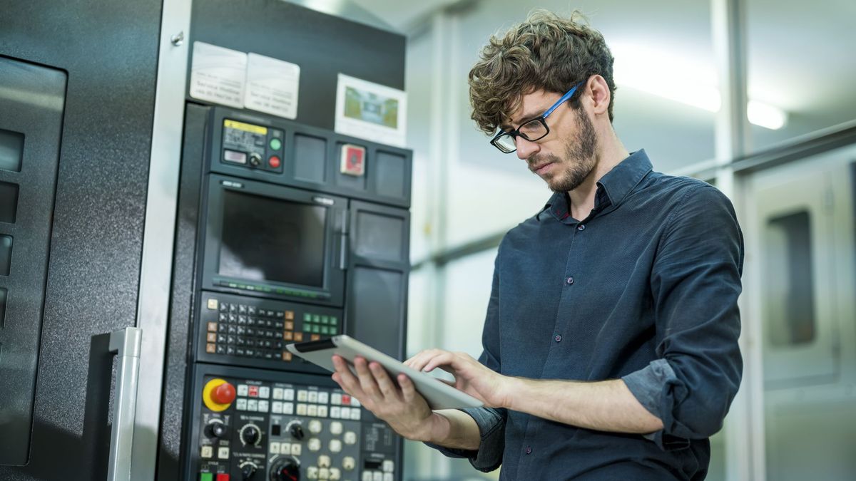 An engineer working on his tablet in front of a machine