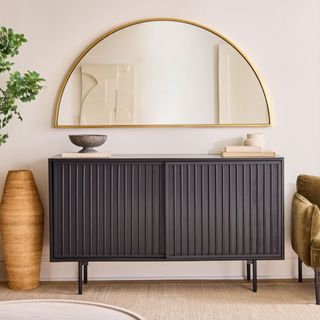 West Elm gold semicircle living room mirror hung above a black ribbed sideboard and styled next to plants and ceramics
