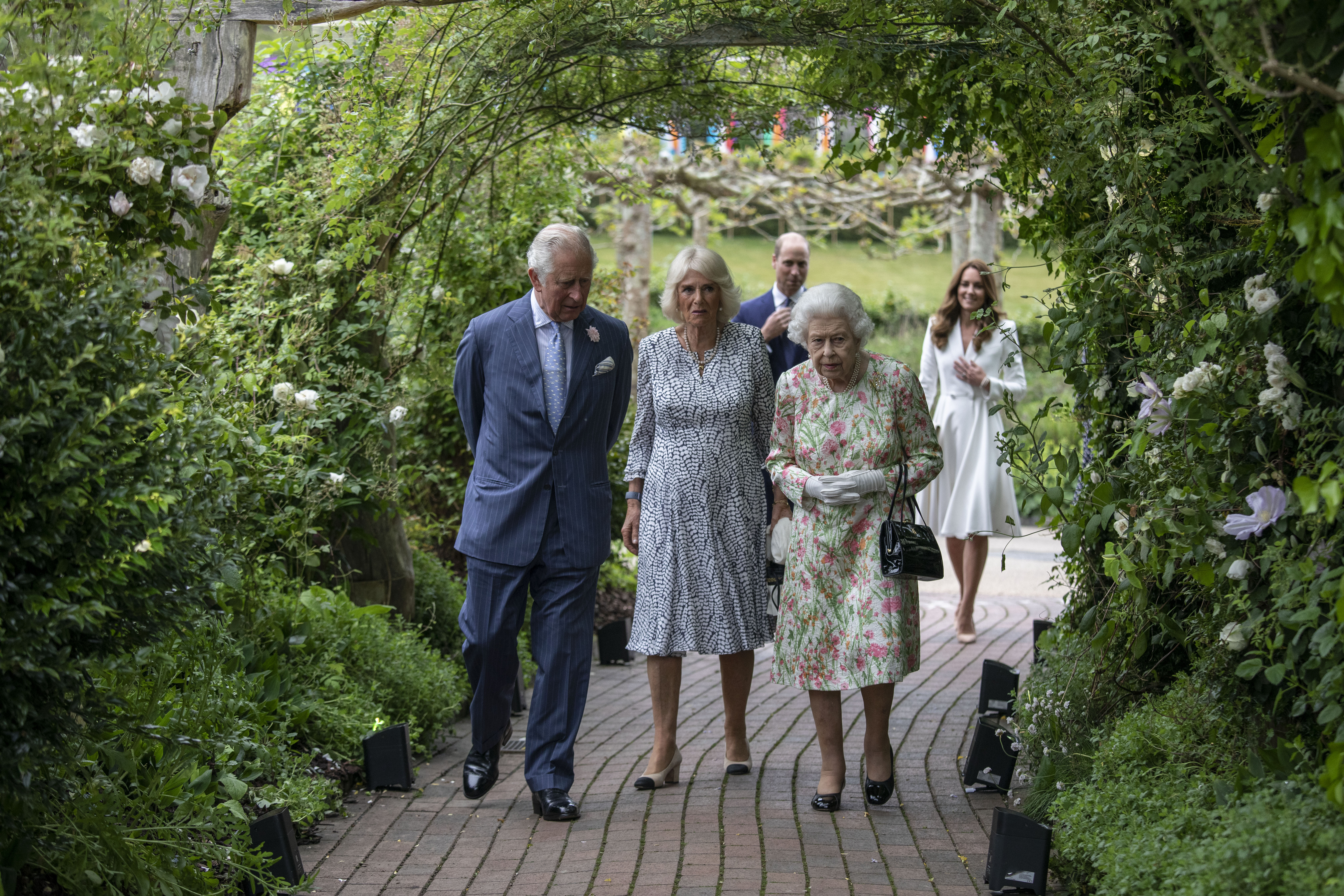 King Charles wears a blue suit and walks alongside Queen Camilla and Queen Elizabeth, who both wear floral dresses