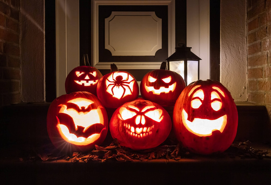 Various pumpkins have been carved and stacked on top of each other on a doorstep. They are lit up in the dark.