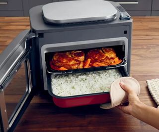 Ninja Combi Multicooker on a wooden countertop with a tray of rice and a tray of chicken inside