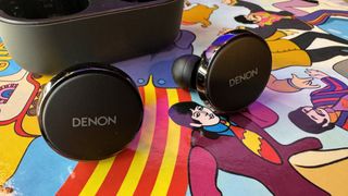 Denon PerL Pro earbuds on a colorful psychedelic background.