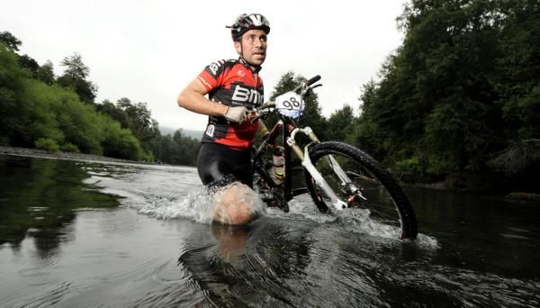 Renzo Corzini (Chile) carries his bike across a river.