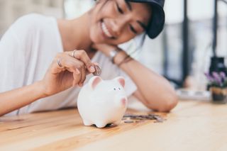 A woman smiles while putting a coin into Piggy Bank - illustrating a guide to collecting and spending Nectar card points