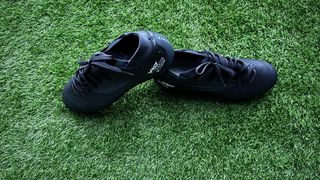 Two black football boots, one heel is resting on top of the other, are back to back on green artificial grass. Kipsta Viralto IV Pro