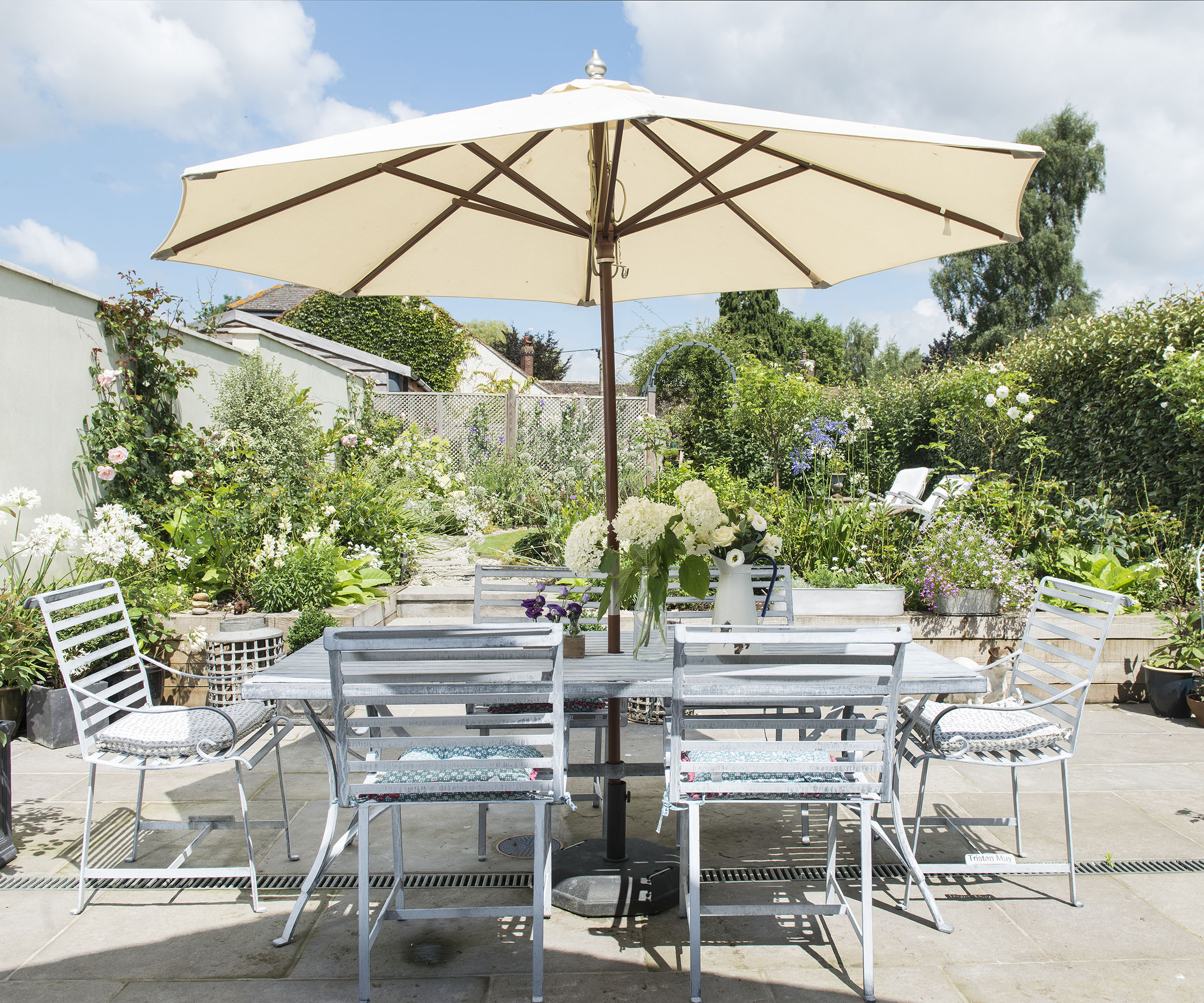 Light outdoor seating area with large white parasol and a metal table and chairs