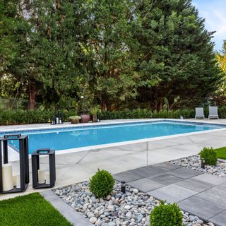 Outdoor swimming pool in garden, surrounded by patio and large trees for privacy