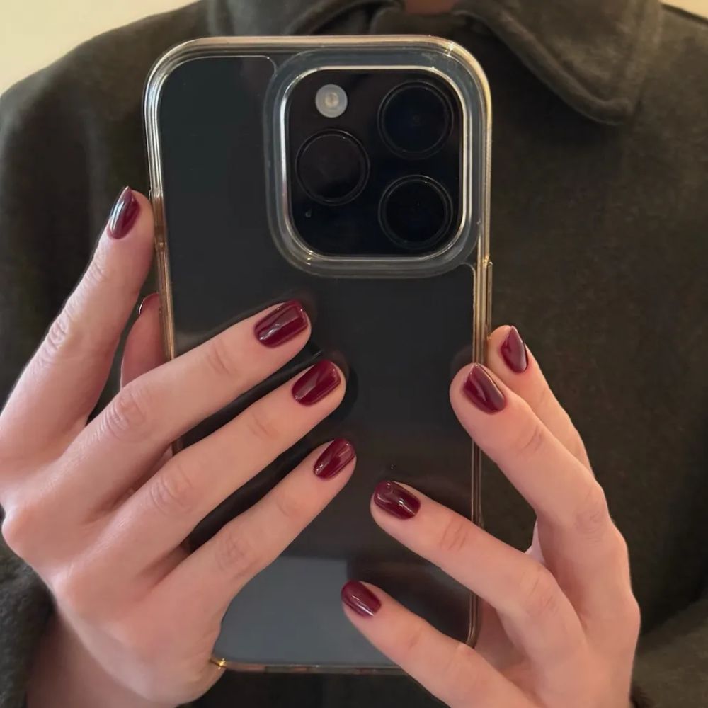 A woman holding an iPhone with a ruby red manicure