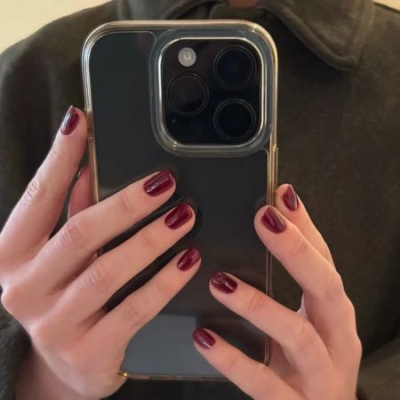 A woman holding an iPhone with a ruby red manicure