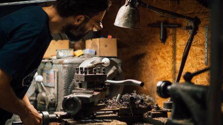 Rubén Duran of Rizzo Cycles leans over his workbench from the side as he works on a custom steel and titanium bike frame.