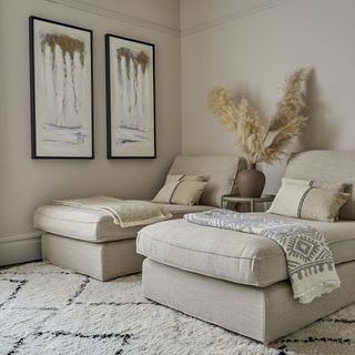 A cream living room with beige loungers, white and grey throws, a large white rug and pampas grass on display