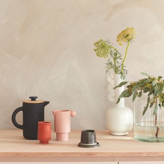 Unfinished plaster wall and a sideboard covered in coffee cups and flower vases