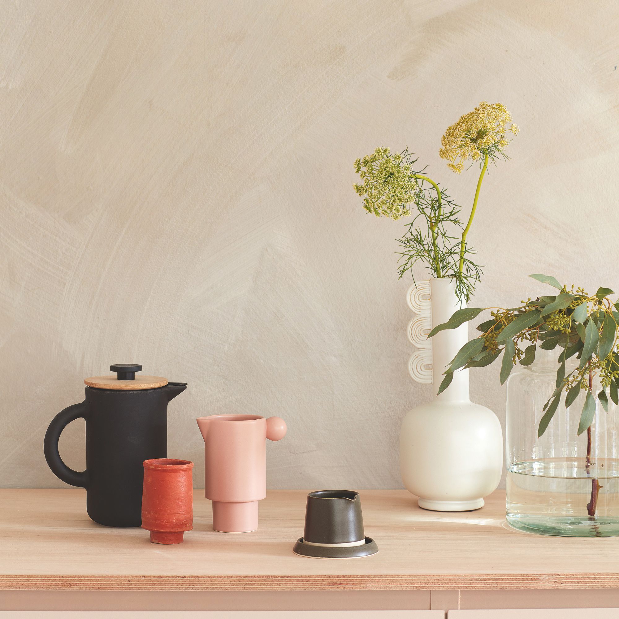 Muro de yeso sin terminar y un aparador cubierto de tazas de café y jarrones de flores