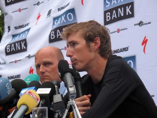 Bjarne Riis watches on as Andy Schleck talks to the media