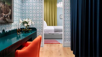 bathroom with teal vanity, orange chairs, navy curtains and a bedroom in the room beyond