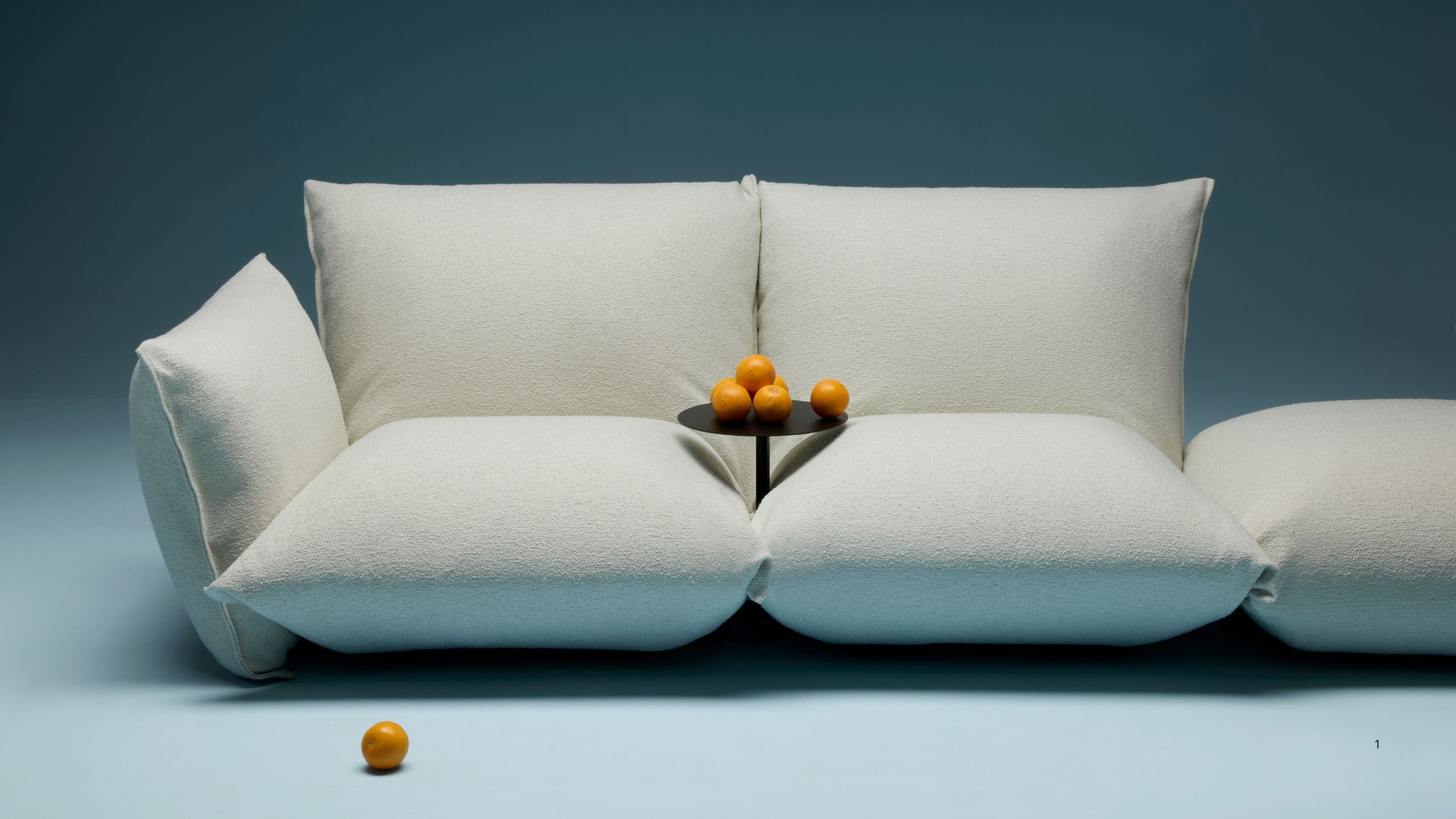 Image of a contemporary, overstuffed style sofa in a white boucle sofa with a side table in between the two cushions. The sofa is styled in an all-blue showroom.