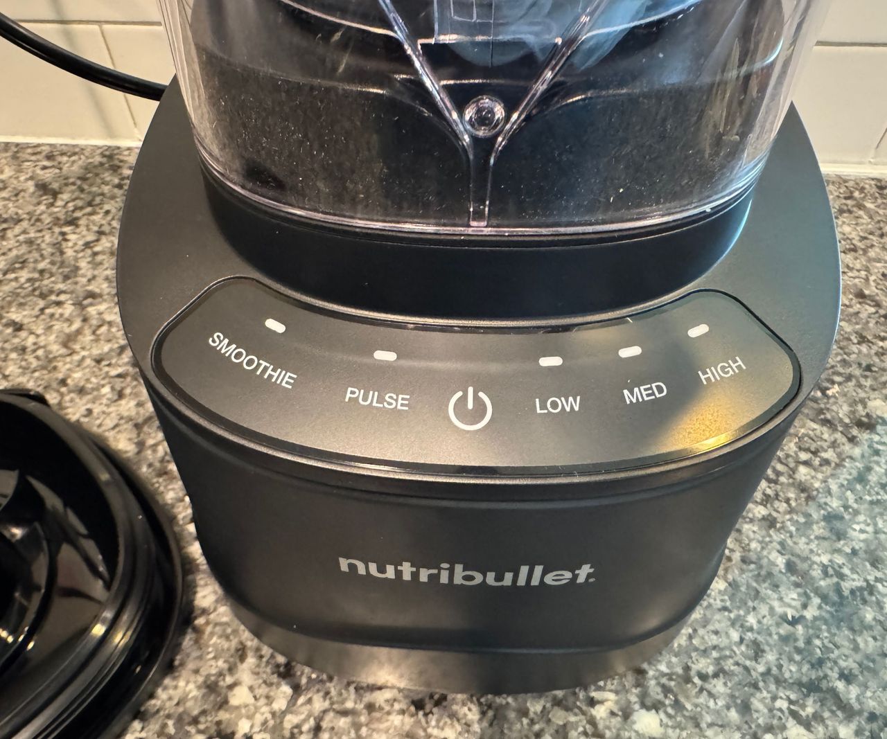 A close up of the base unit of a nutribullet PowerCore XL Blender on a stone kitchen counter against white subway tiles.