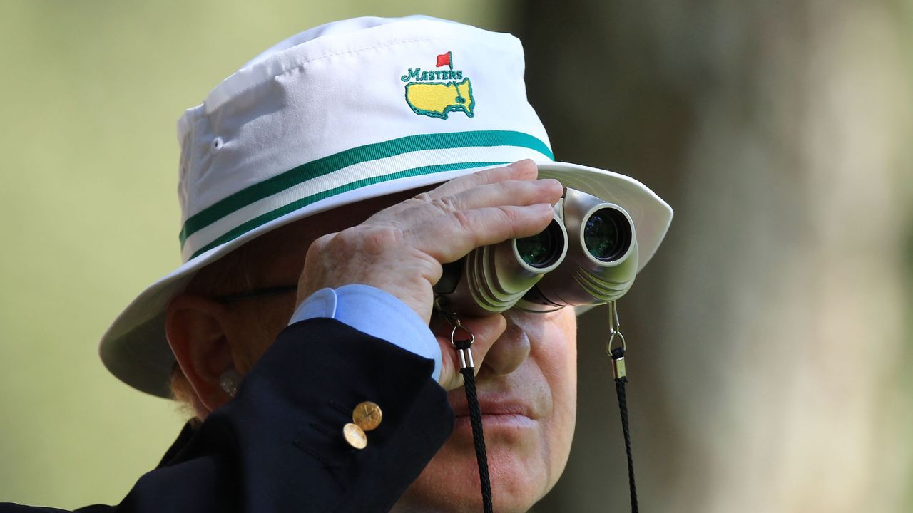 A Masters patron wearing a white Masters bucket hat looking through binoculars