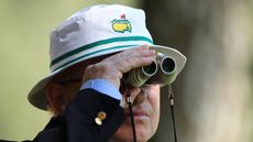 A Masters patron wearing a white Masters bucket hat looking through binoculars