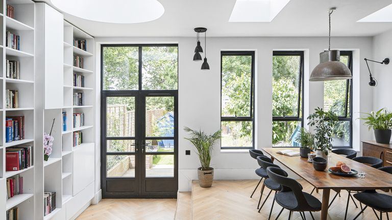 Rear extension with black metal French doors and contemporary windows, ceiling-to-floor built-in bookshelves painted white, and mid-century dining furniture