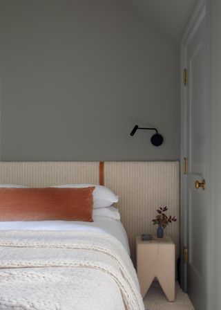 Grey bedroom with orange velvet cushions and striped headboard