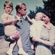 Prince Philip holding Prince Charles while Princess Anne, held by Queen Elizabeth, pulls on his lip