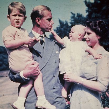 Prince Philip holding Prince Charles while Princess Anne, held by Queen Elizabeth, pulls on his lip 