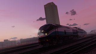 Train riding past a city with a pink sky in the background.