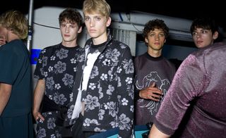 Guys wearing Man S/S 2015 collection. The two guys on the left are wearing a navy / floral design. Next to them is a guy wearing a purple shirt with a white design on the front