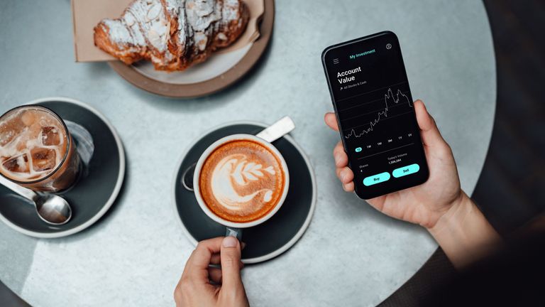 high angle view of a young woman checking the stock market on smartphone, having breakfast at coffee shop business on the go concept