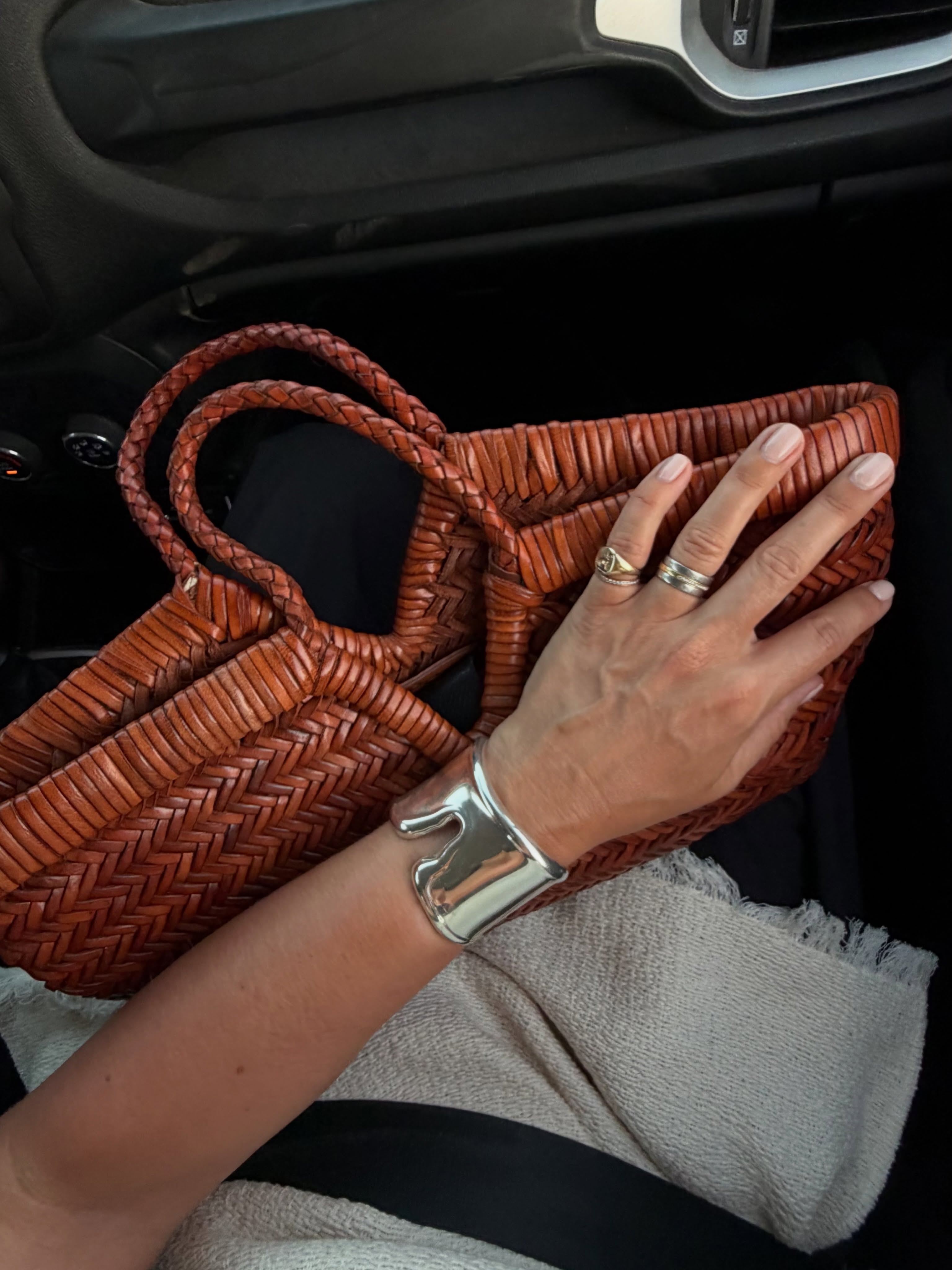 An image of @alexisforeman wearing a silver arm cuff with a woven leather bag.