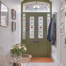 Olive green front door with stained glass panels in hallway.