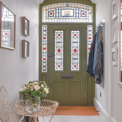 Olive green front door with stained glass panels in hallway.