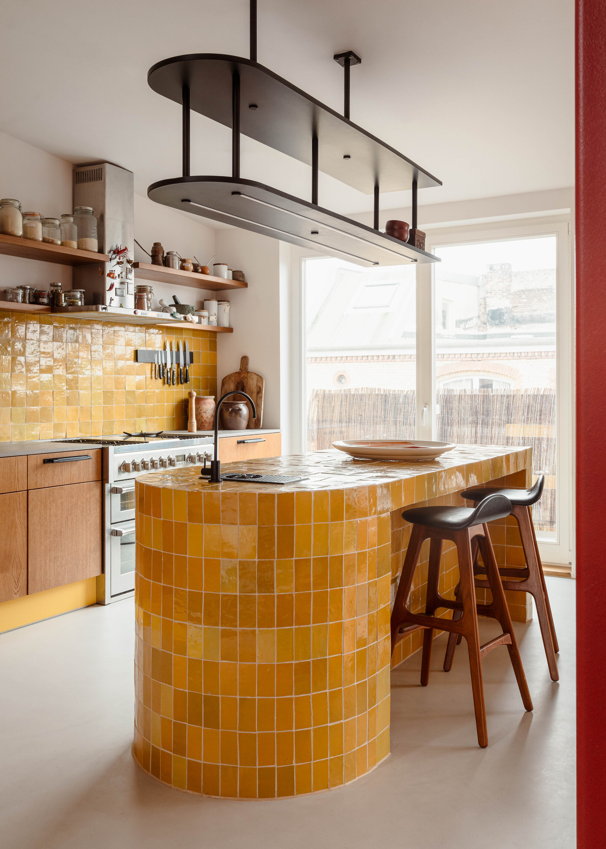 A kitchen with a yellow tiles backsplash, and a curved island wrapped in the same yellow tiles