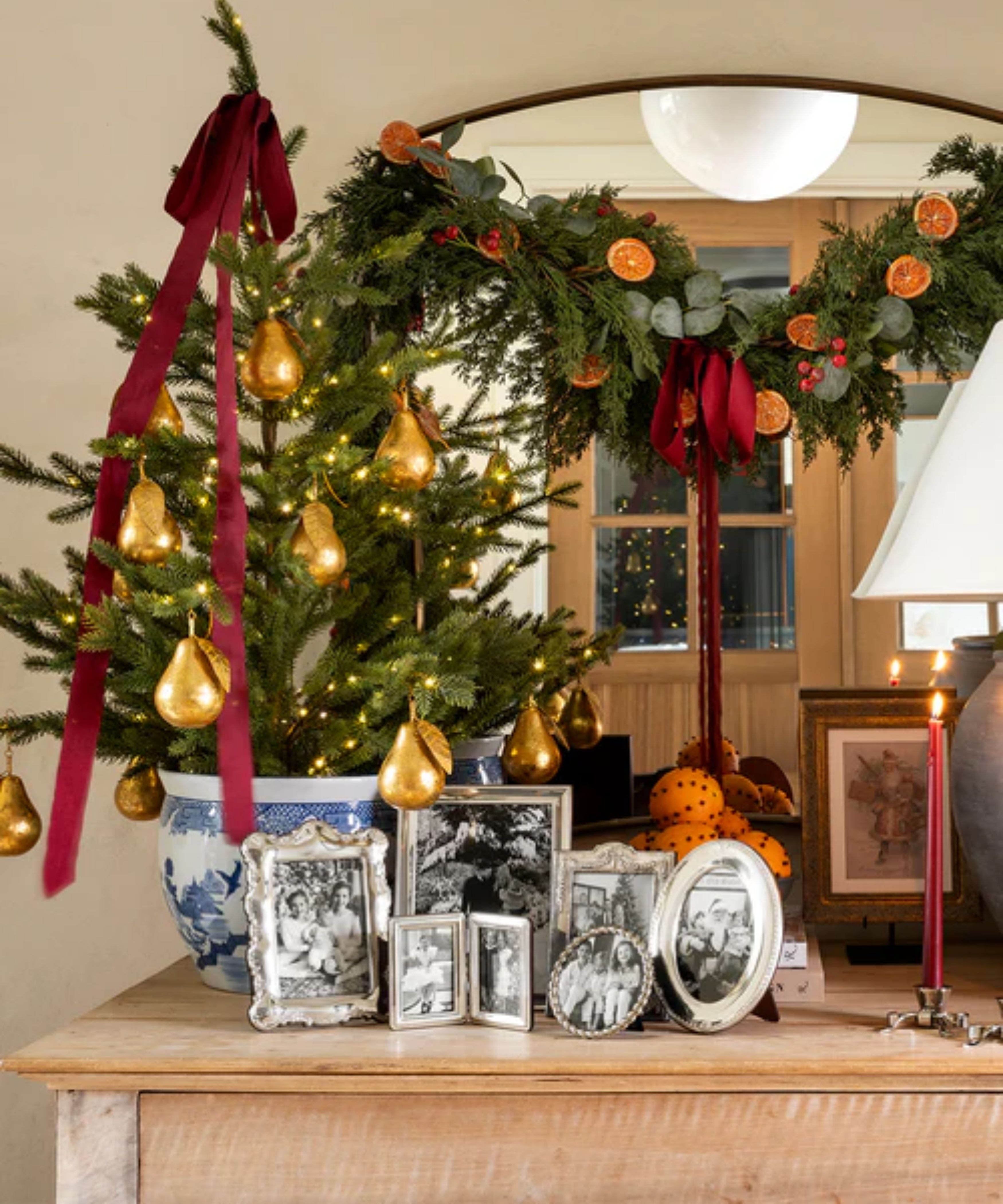 mcgee and co christmas entryway credenza styled with a mini christmas tree in a chinoiserie pot, styled with gold pear ornaments, red ribbon, a garland with oranges and mini silver photo frames