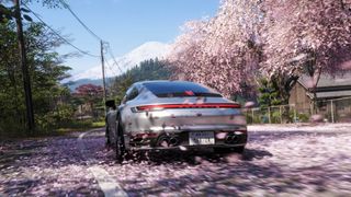 Cherry blossoms swirl around a silver car that drives towards Mt Fuji in Forza Horizon 6