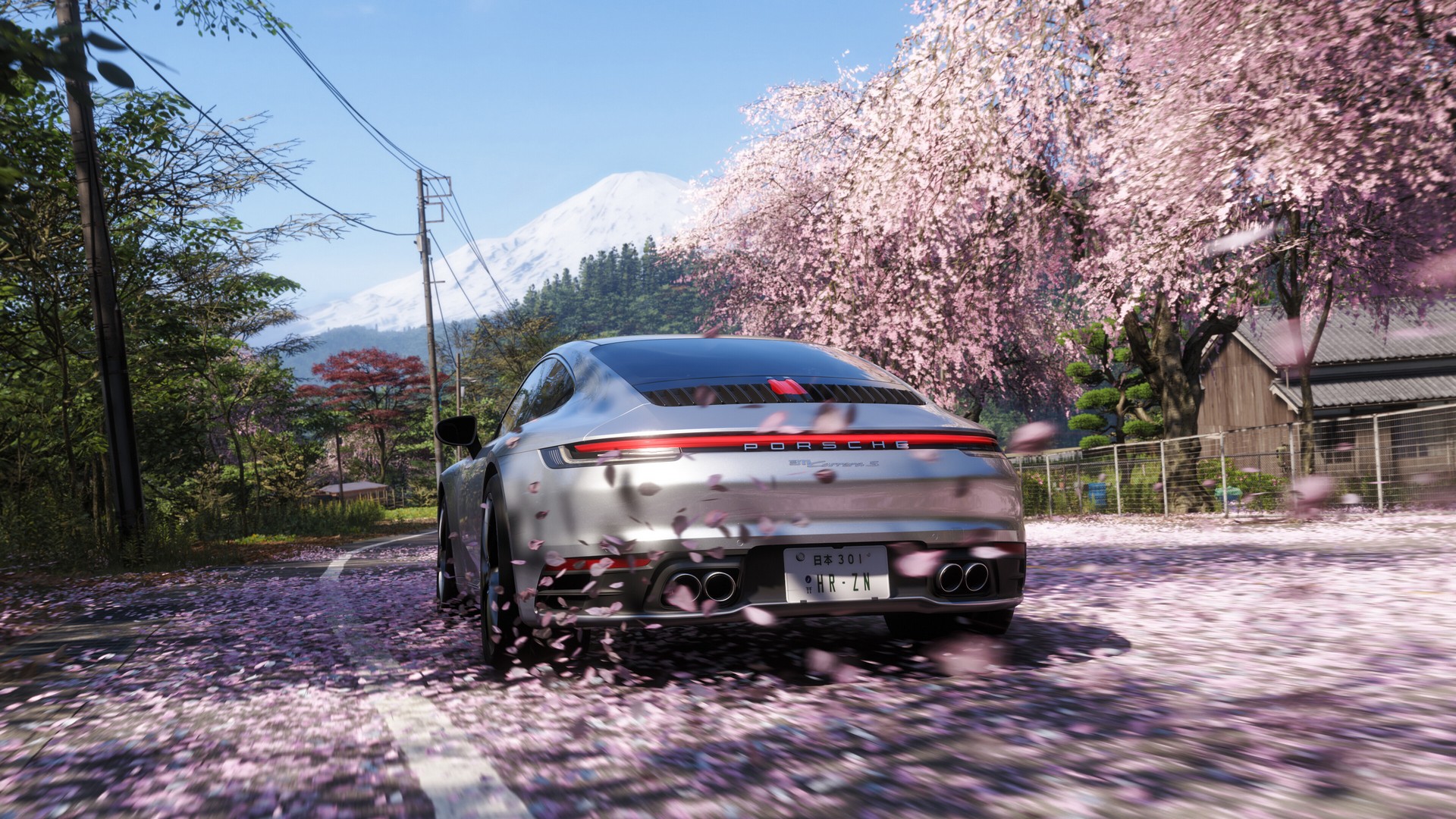 Cherry blossoms swirl around a silver car that drives towards Mt Fuji in Forza Horizon 6