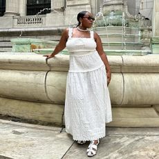 Aniyah wears white dress and white fisherman sandals while posing in front of a large fountain