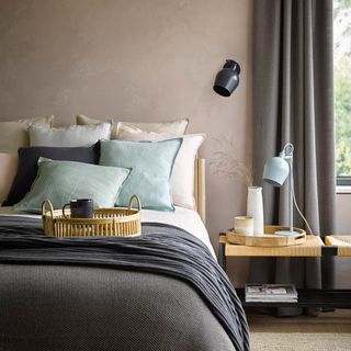 how to decorate a guest bedroom, bedroom with plaster walls, brown curtains and throw, aqua and pastel pink cushions, bench as a side table, table lamp and wall light, trays