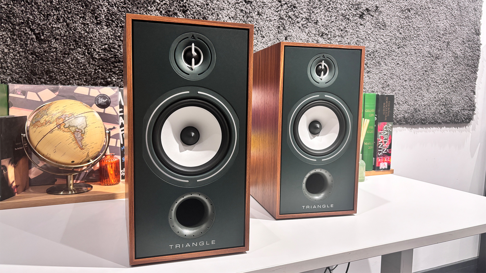 Triangle Borea BR04 standmount speakers on white table in front of busy bookcase