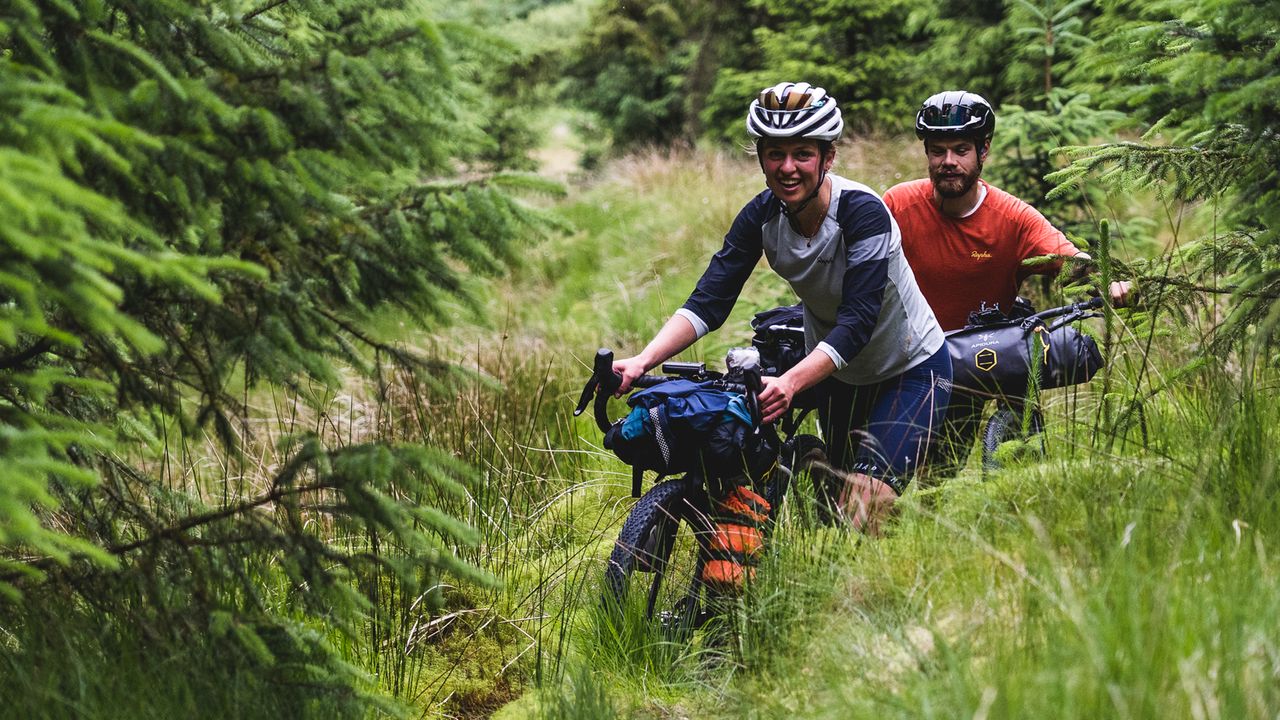 Two cyclists pushing through dense undergrowth