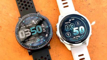 Close-up of the Amazfit Active Max next to the Garmin Forerunner 570 on a bright orange table