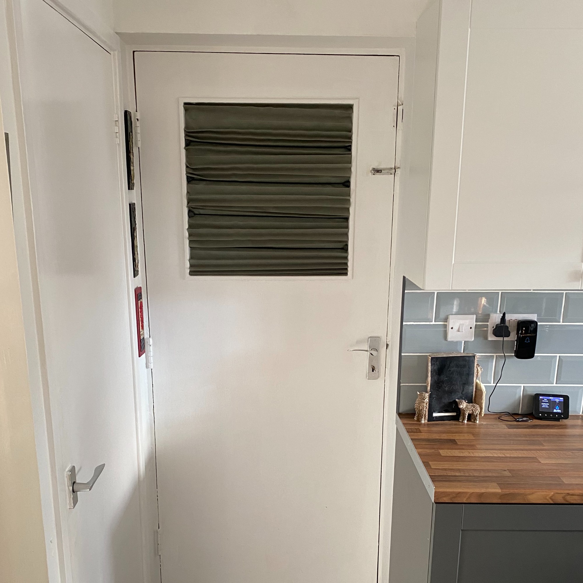 The old painted timber door with single glazed glass panel (with makeshift pleated blind) that leads from the kitchen to the attached garage