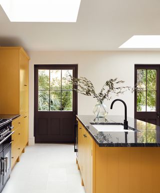 kitchen island color ideas, yellow and white kitchen with black crittall doors, yellow kitchen island, black countertops, skylights, white flooring