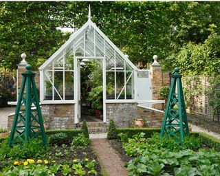 Greenhouse filled with container plants with vegetable garden in front of it
