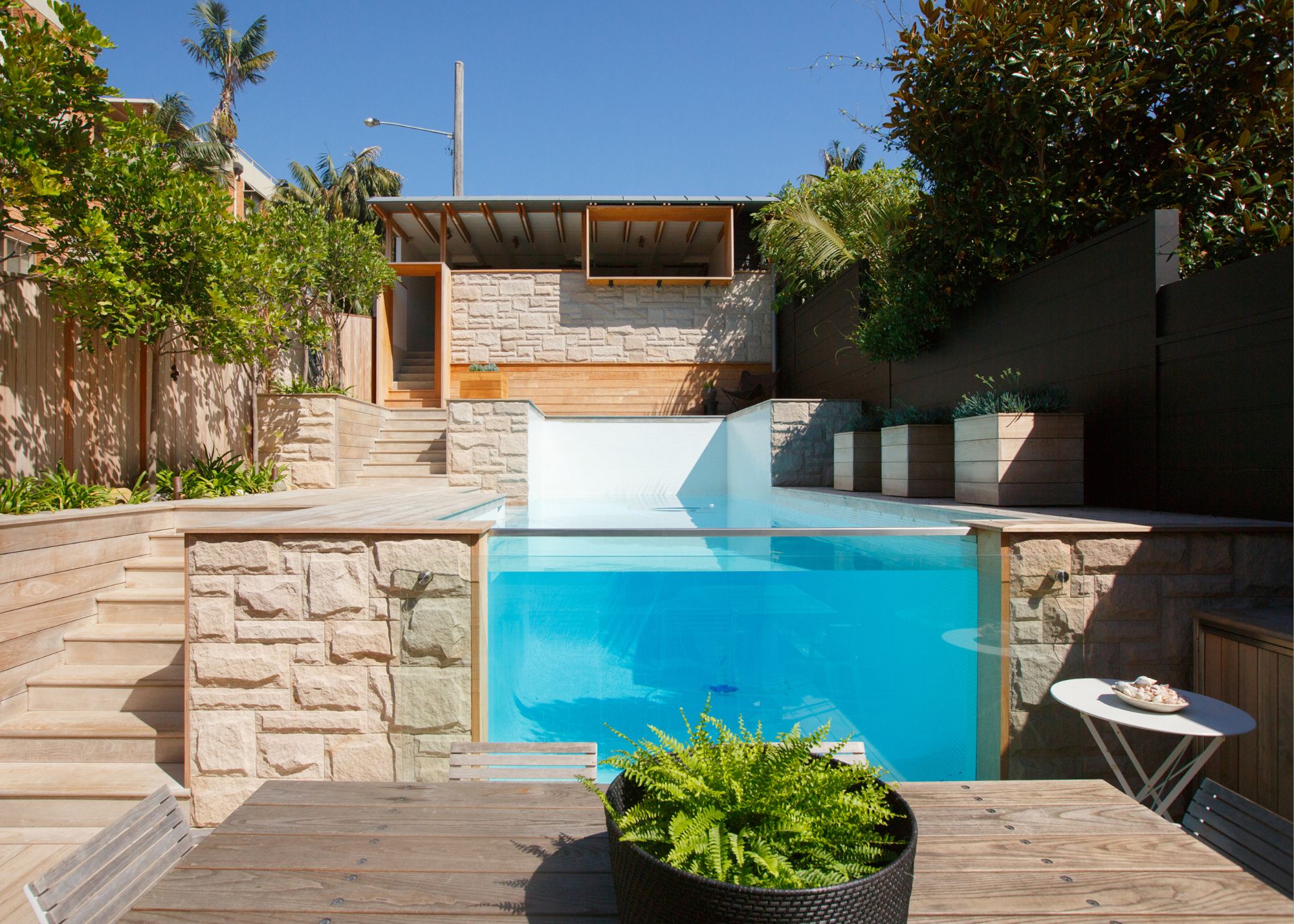 A small glass fronted pool in a backyard with a dining table in front