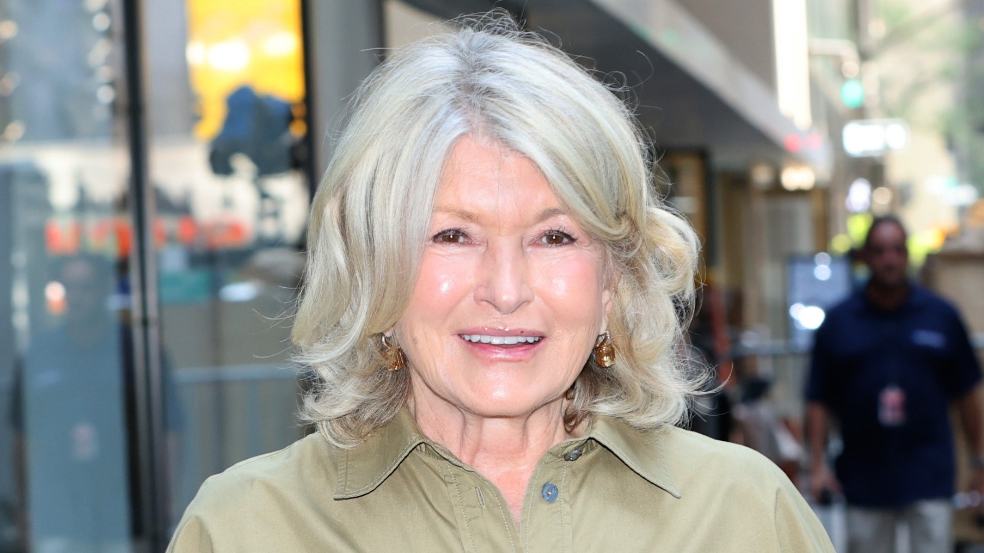 Image of Martha Stewart smiling with blonde curled shoulder-length bob and wearing a khaki beige shirt