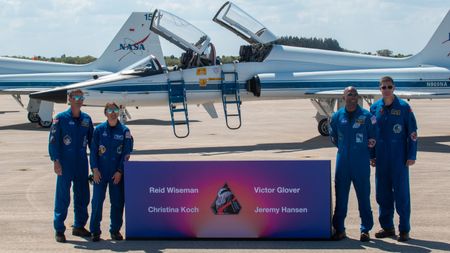 Four people wearing blue jumpsuits stand next to each other in front of a NASA jets.