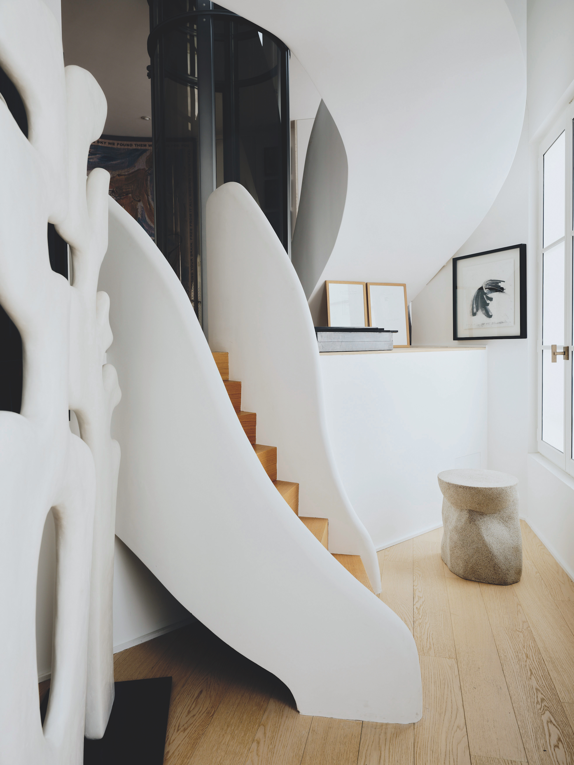 A white, curved staircase with warm toned wooden stairs and floors.